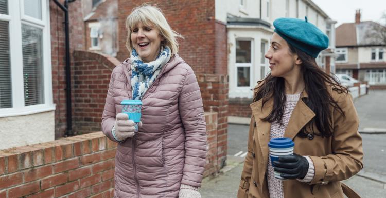 women_walking_down_the_street_talking_and_drinking_coffee