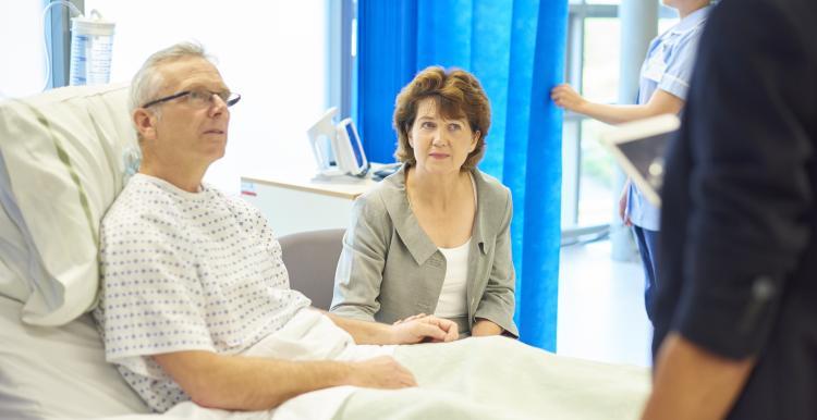 Man_sitting_in_a_hopsital_bed_with_a_woman_visitor_at_his_side_listening_to_a_doctor