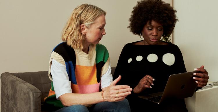 Two_women_sitting_on_a_sofa_talking_and_looking_at_a_laptop