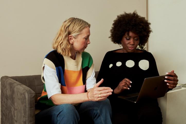 Two_women_sitting_on_a_sofa_talking_and_looking_at_a_laptop