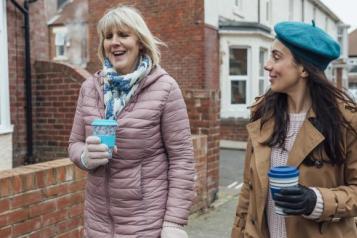 women_walking_down_the_street_talking_and_drinking_coffee